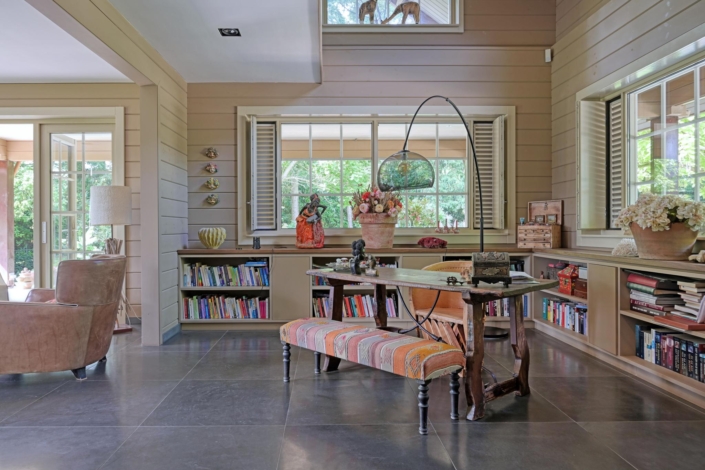 Gezellige studeerkamer met houten wanden, kleurrijke gestreefd bankje aan bureau. Planken links en rechts vol boeken en decoraties. Grote ramen brengen veel natuurlijk licht binnen. Leren stoel in de hoek. Finnhouse.nl. - Finnhouse