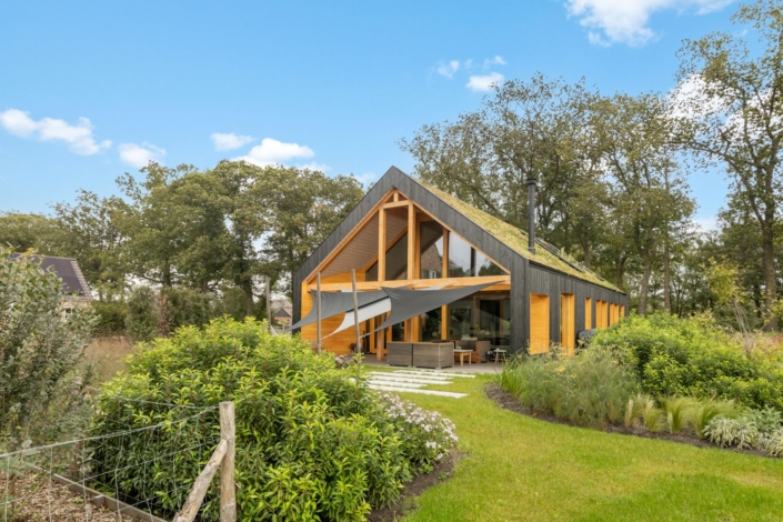 Modern huis met driehoekig dak, houten accenten en grote glazen ramen langs door weelderig groen. Zonneschermen trekken zich uit over een terras, betrouwbare lucht met enkele wolken. - Finnhouse