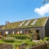 Modern zwart houten huis met groen dak, bedekt met vegetatie en zonnepanelen. Grote ramen uit kijken op een aangelegde tuin, een klein terras en een groentetuin onder blauwe lucht. - Finnhouse