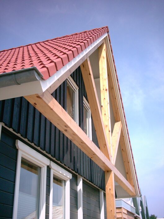 Receptiegebouw Renesse-stijl huis met moderne architectuur, hellend rood pannendak en donkere verticale gevelbekleding. Grote houten driehoekige balken met de daklijn; rechthoekige ramen afmetingen de tweede verdieping. - Finnhouse