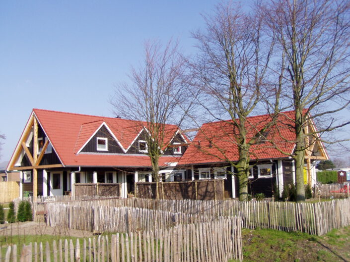 Een traditioneel zwart-witte Finnhouse met rode zadeldaken en dakkapellen, naast door kale bomen en een rustiek houten hek, tegen een zwakke blauwe lucht. - Finnhouse