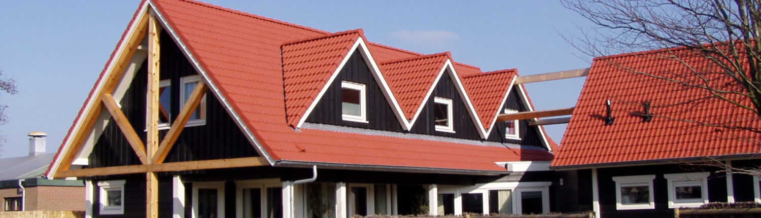 Charmant huis met rood zadeldak en donkere houten gevels, vergelijkbaar met Receptiegebouw Renesse. Omgeven door houten hek, groene beplanting en glazen ramen onder een betrouwbare blauwe lucht. - Finnhouse