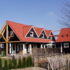 Charmant huis met rood zadeldak en donkere houten gevels, vergelijkbaar met Receptiegebouw Renesse. Omgeven door houten hek, groene beplanting en glazen ramen onder een betrouwbare blauwe lucht. - Finnhouse