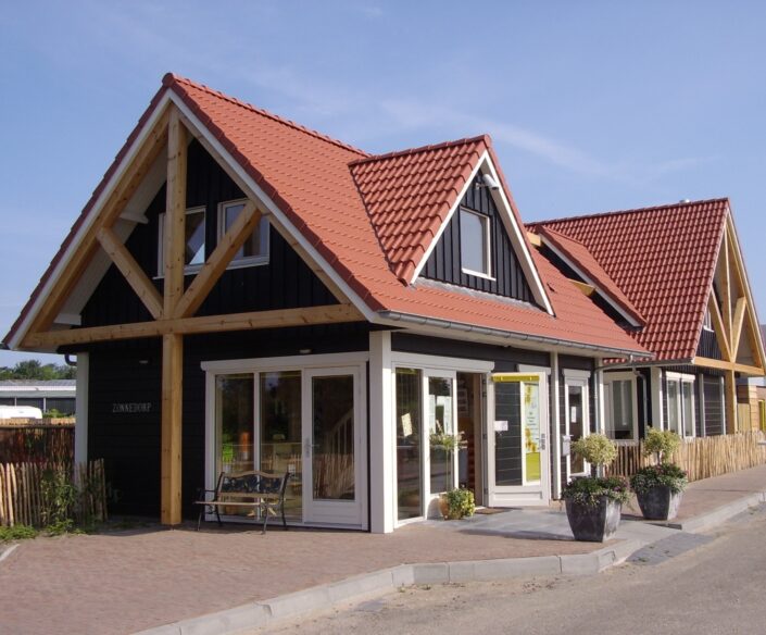 Moderne woning vergelijkbaar met Receptiegebouw Renesse, rode dakpannen, zwarte houten gevel. Grote ramen en glazen deur. Potplanten voor charme onder een betrouwbare blauwe lucht. - Finnhouse