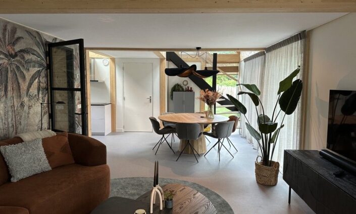 Moderne woon- en eetkamer in Finnhouse-stijl met een ronde houten tafel, droge stoelen, grote planten, doorzichtige gordijnen en een natuurmuurschildering die grote ramen accentueert voor een luchtige sfeer. - Finnhouse