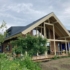 Modern houten Finnhouse met stalen A-frame dak en grote ramen in een duurzame groene omgeving. Overdekt door bomen en planten, met een terras en tuinmeubels aan de voorkant. - Finnhouse