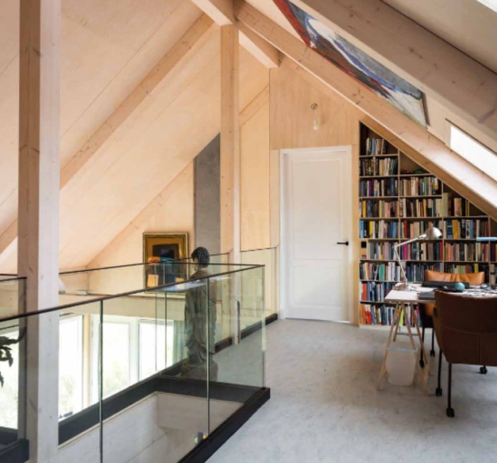 Moderne zolderkamer met houten schuine plafonds en glazen balustrade, witte deur, boekenkast en groot groen kunstwerk. Zonovergoten bureau naast hoge ramen stimuleert creativiteit. Vind inspiratie op Finnhouse.nl. - Finnhouse