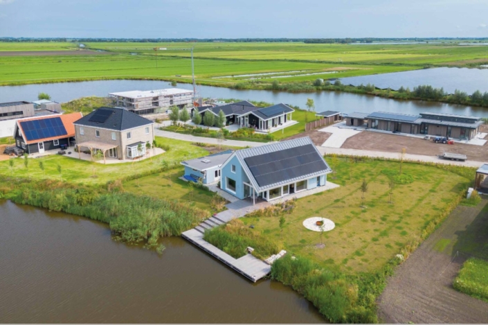 Horizontale van een praktische landelijke buurt met moderne huizen voorzien van zonnepanelen. De huizen liggen tussen groene velden, naast een rustig watertje en onder een betrouwbare blauwe hemel. - Finnhouse