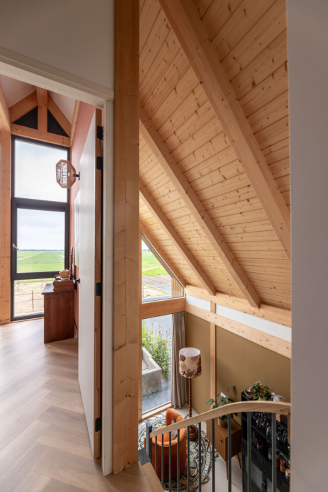 Modern huisinterieur met houten gewelfd plafond, grote ramen met schilderachtig uitzicht. Inclusief wenteltrap en knusse zithoek met oranje stoel, ideaal voor gezinsmomenten in een lichte, ruime setting. - Finnhouse