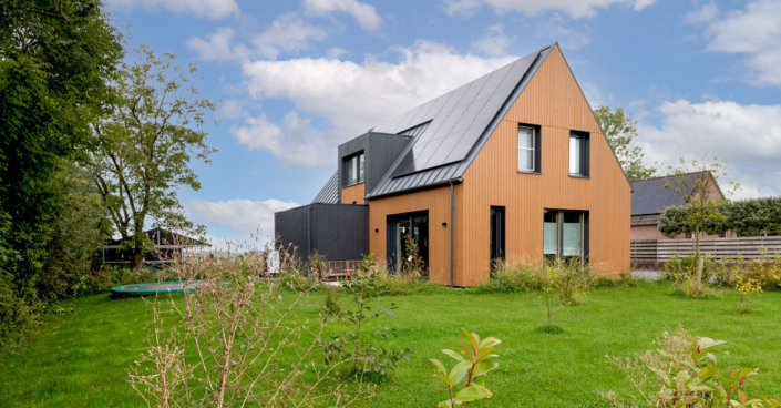Moderne houten woning met zonnepanelen, ideaal voor een gezin, verborgen door een groene tuin met struiken en bomen. De deels bewolkte lucht creëert een serene sfeer. Finnhouse duurzame architectuur. - Finnhouse
