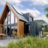 Moderne houten Finnhouse met zwarte panelen, grote ramen en zonnepanelen op het dak. Voorgrond toont patio met tuinmeubilair, binnenplaats groen onder een deels bewolkte hemel. Perfect voor een gezin. - Finnhouse