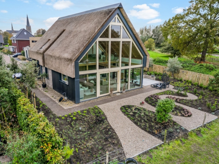 Modern Finnhouse met een rieten dak en grote glazen ramen in een groene omgeving. Perfect voor gezinnen die houden van natuur en duurzame architectuur. Grindpad leidt door de tuin vol jonge planten. - Finnhouse