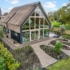 Modern Finnhouse met een rieten dak en grote glazen ramen in een groene omgeving. Perfect voor gezinnen die houden van natuur en duurzame architectuur. Grindpad leidt door de tuin vol jonge planten. - Finnhouse