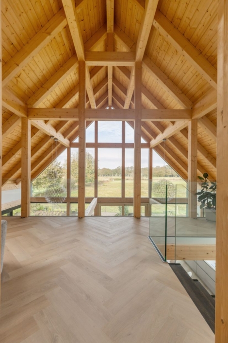 Moderne loft met hoog, houten gewelfd plafond en grote ramen die uitkijken op groen landschap. Lichte houten visgraatvloer en glazen balustrade maken het ideaal voor een gezin. Finnhouse-stijl. - Finnhouse