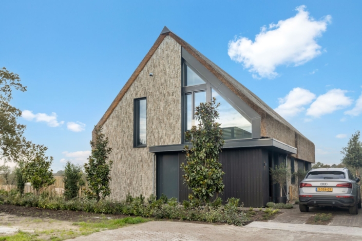 Moderne woning met stalen schuin dak, baksteen en houtmix gevel. Grote ramen voor veel lichtinval. Goed onderhouden tuin, auto oprit onder deels bewolkte blauwe lucht. Perfect familieverblijf. - Finnhouse
