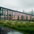 Modern, langwerpig kantoorgebouw van Finnhouse met grote glazen ramen en houten panelen in een mistig, groen landschap. Het gebouw heeft een schuin dak en wordt omringd door gras, bomen en een natte weg. - Finnhouse