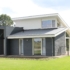 Moderne Finnhouse bungalow met donkergrijze en witte buitenkant, grote ramen en schuin dak. Voortuin met strak gemaaid gras, omlijst door bomen en een veld op de achtergrond. - Finnhouse